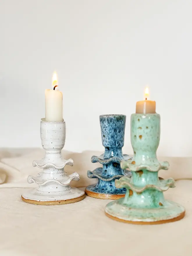 three ceramic candlestick holders in white, blue, and green, two of which are holding lit candles