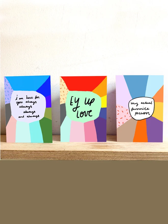 Three cards sit on shelf, all colourful designs by Nicola Rowlands.