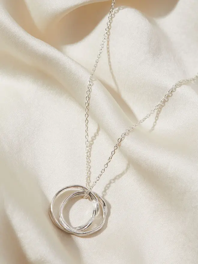 Silver Entwined Circles Necklace draped over a silk material