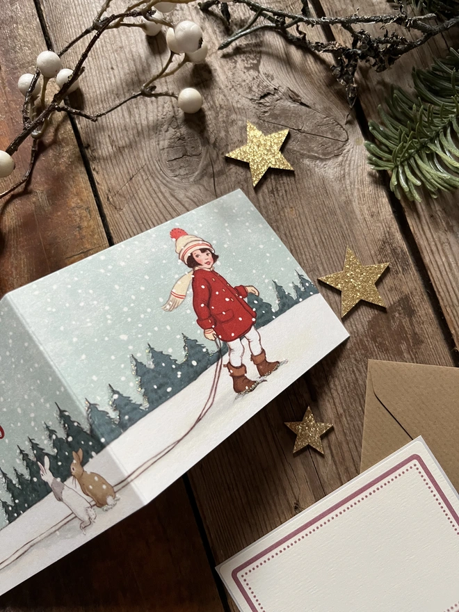 a close up of a traditional Christmas greeting card featuring a traditional story book style illustration of a little girl in a red coat