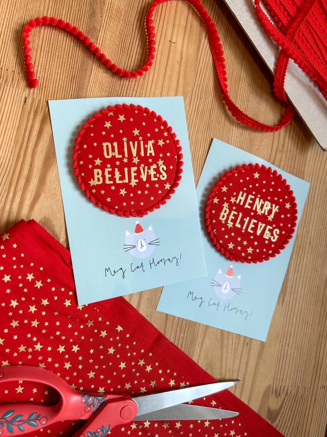 Red christmas 'Believe' badges with gold stars and a red pom pom trim and a child's name 