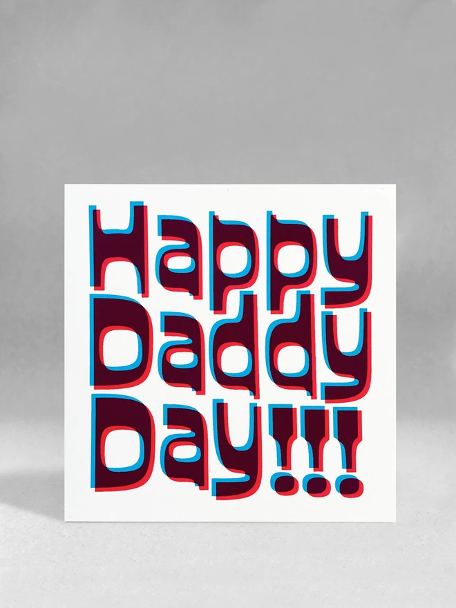 Happy Daddy Day printed in magenta and cyan blue ink, a slight overlapped design to create this retro jolly card. Stood on a white studio background.