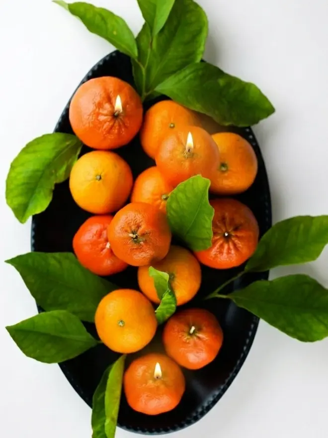 Christmas Satsuma Candle. a stack of candles shaped like satsuma oranges in a round black dish.