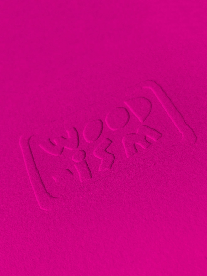 A close up on an embossed logo on bright pink paper