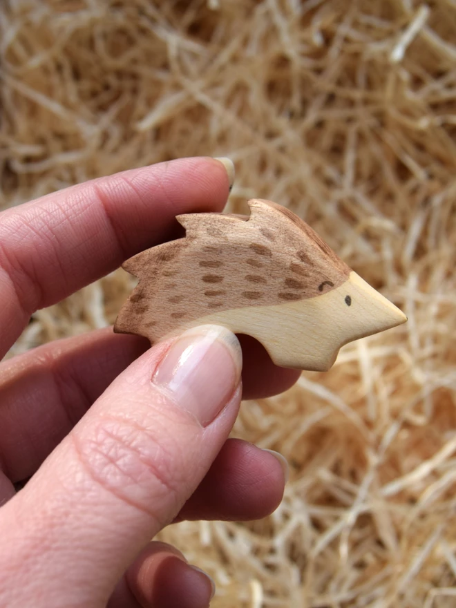 wooden toy hoglet held above woodwool