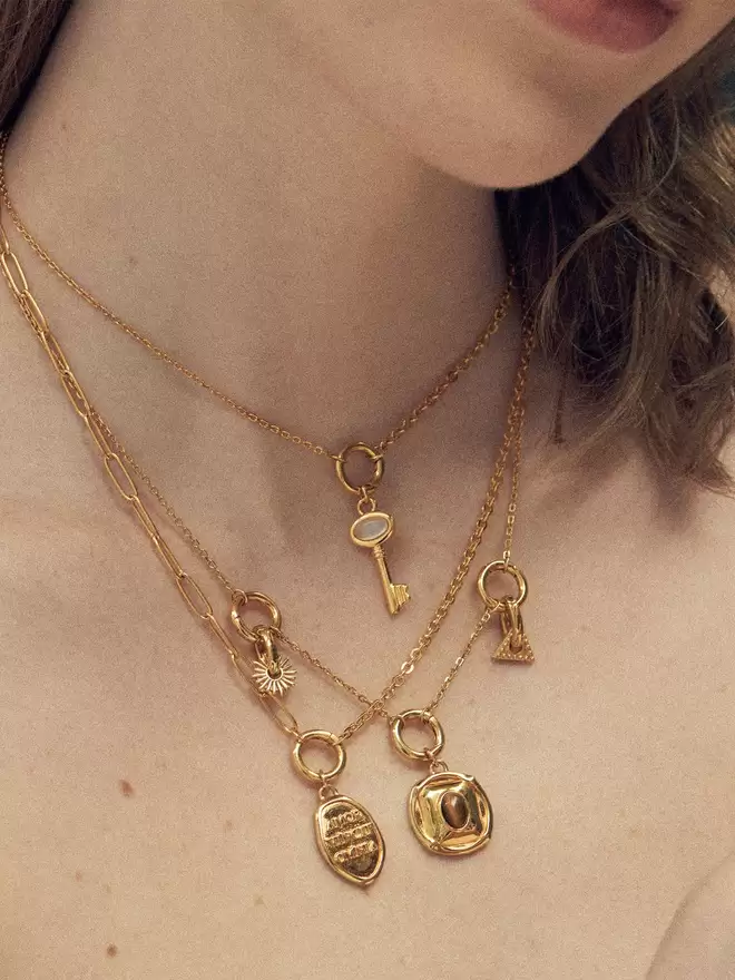 woman wearing three gold necklaces styled with a mix of gold pendants and charms