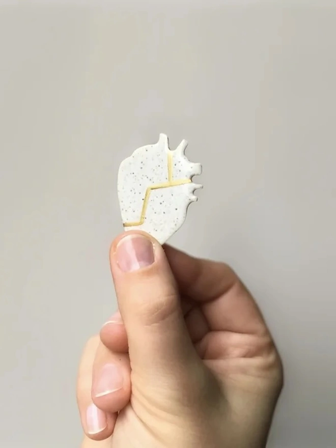 (Un)Broken Heart Pin, a person holding a white and golden heart pin. 