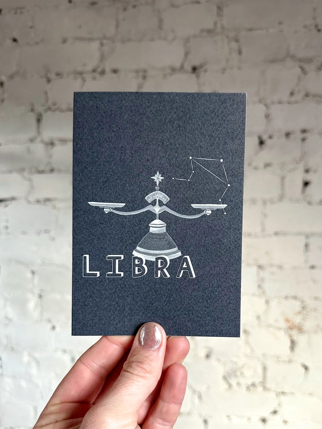  a greetings card featuring a greyscale illustration of a zodiac style set of scales with the text “LIBRA”