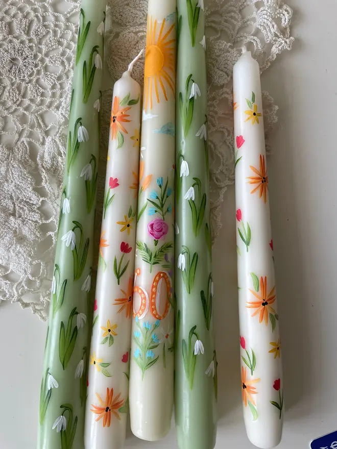 Birthday Or Anniversary Hand Painted Candle, a group of colourful candles resting against a white surface. A candle with a number written on it can be seen in the middle. 