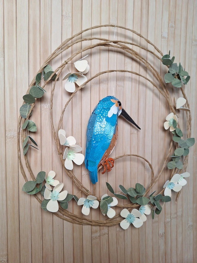 Back side view of a handmade floral wreath featuring a paper sculpture of a kingfisher
