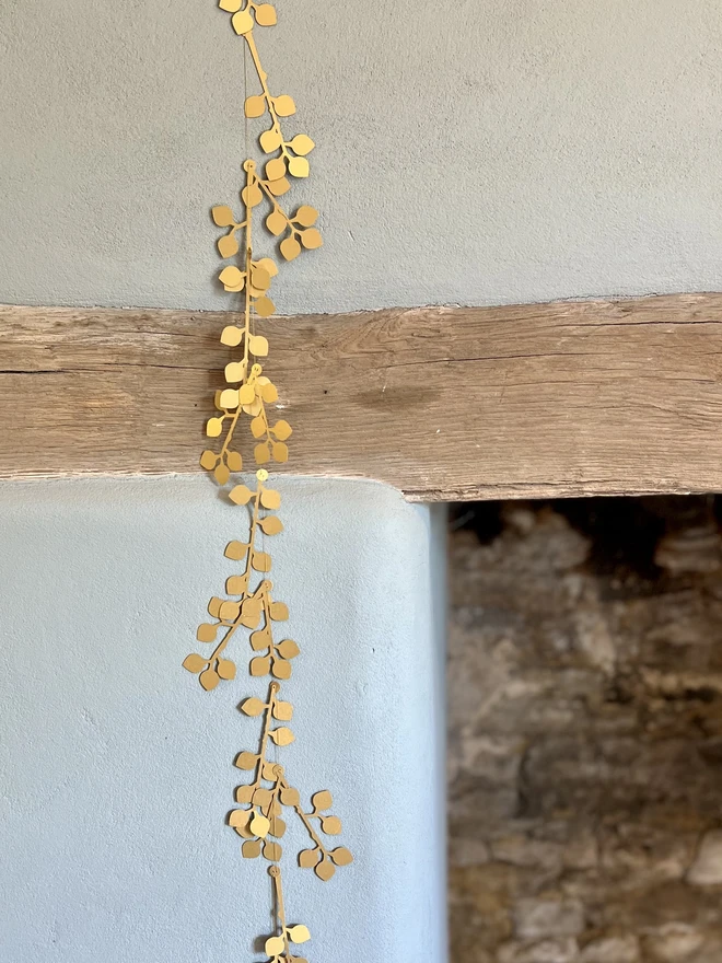 Gold Berry Garland hung vertically on a neutral limewash wall next to fireplace