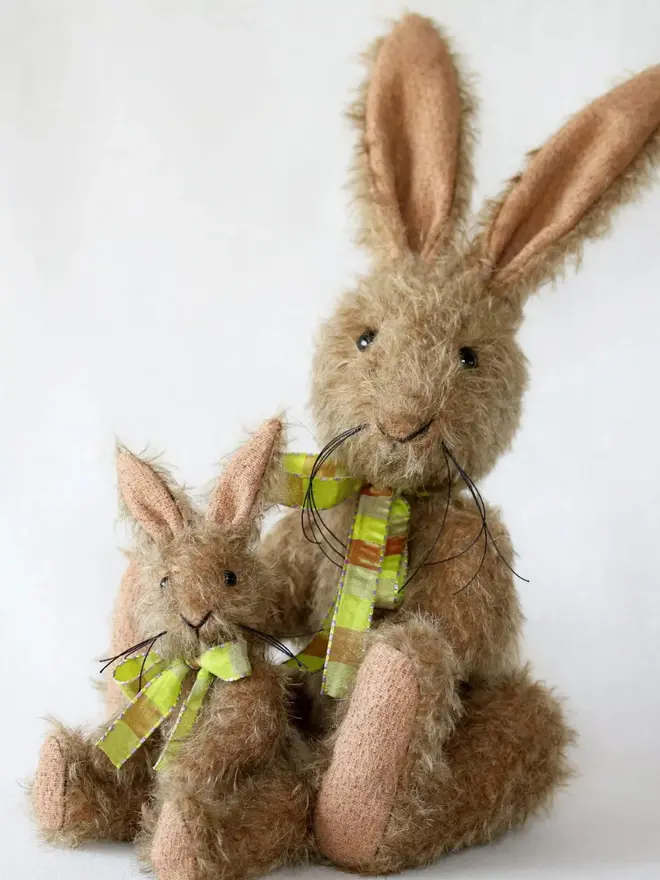 Handmade brown stuffed rabbit with long ears and a green ribbon bow sitting upright with a small bunny against a plain background