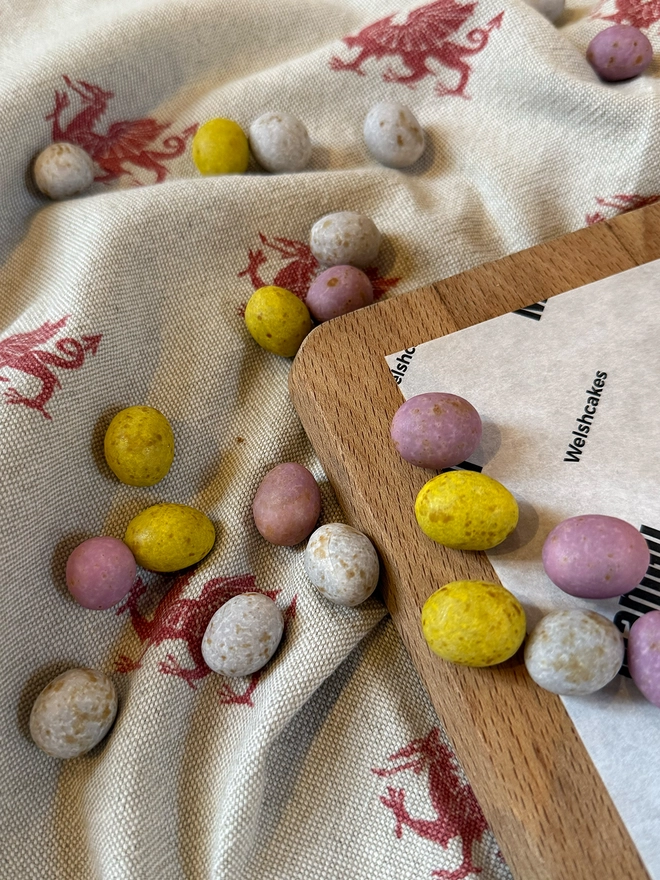 loose mini eggs on a beige and red welsh dragon table cloth next to a wooden chopping board on the right side