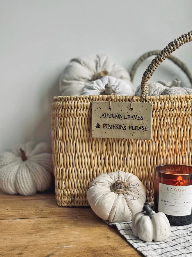 woven basket filled with fabric pumpkins with a ceramic sign hung on the outside 