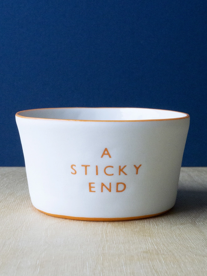 Ceramic porcelain pudding bowl with A Sticky End written on the side. A white fruit bowl with orange rim.