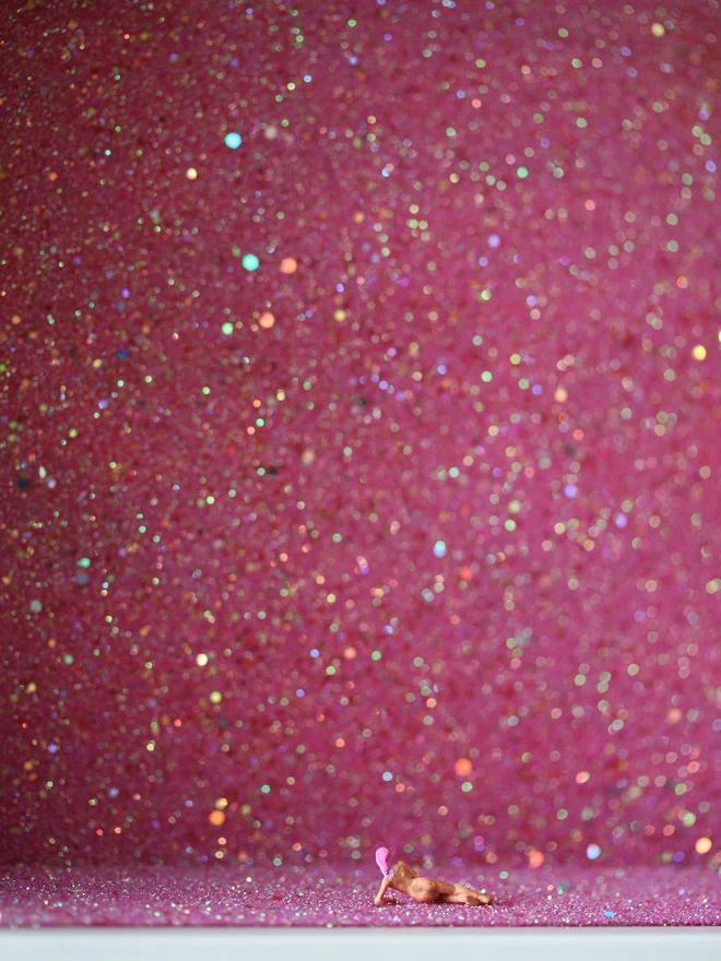 A tiny naked woman with pink hair lies contemplating a sparkling pink interior (close up)