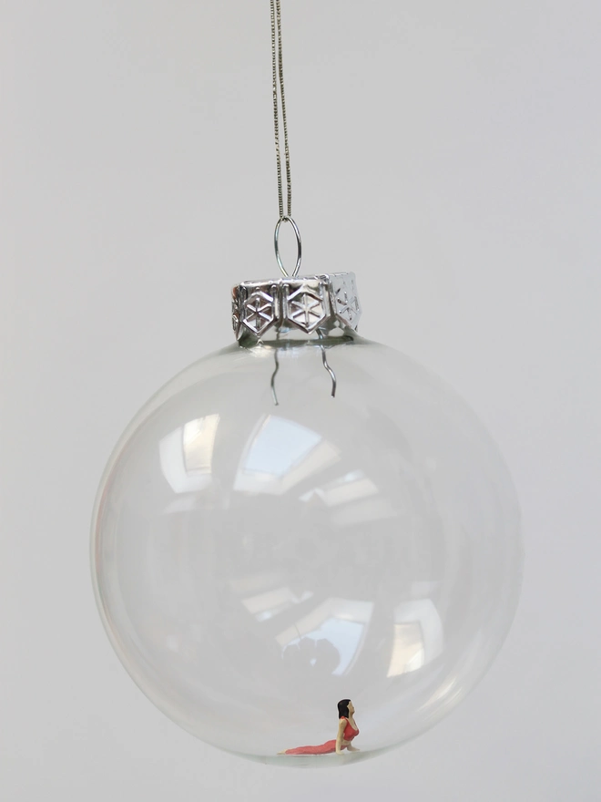 Miniature figure of a female doing a Sphninx yoga pose, in a glass hanging christmas bauble 