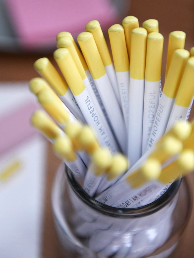 A glass jar full of white pencils with yellow tips and the words "Today I Am Hopeful" along the side of each one.