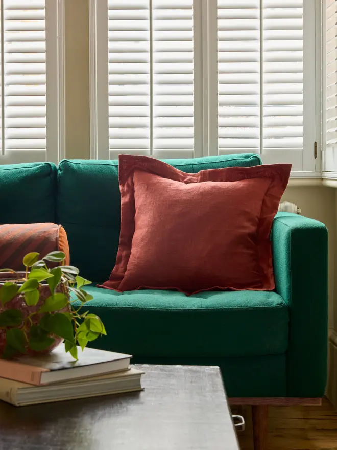 Handmade rust classic linen oxford cushion 45x45cm with feather pad on teal sofa, Kika Bespoke