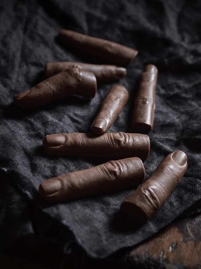 Realistic milk chocolate human fingers on dark cloth background