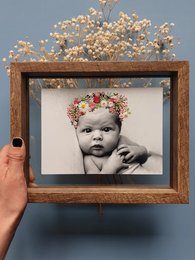 Baby photo with hand embroidered pinks and white flower crown, held in double glass frame