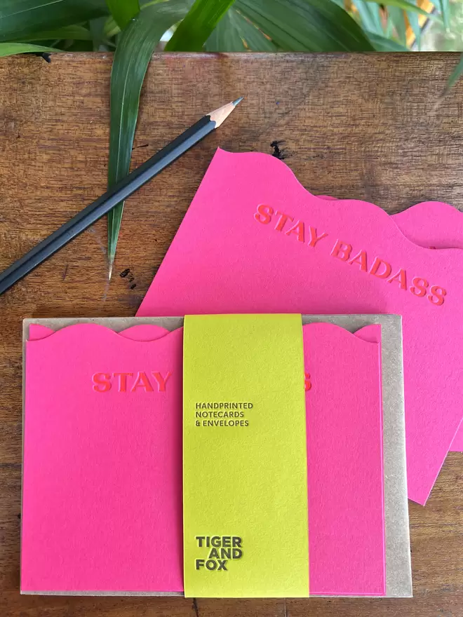 Stay Badass letterpress printed in orange ink on bright pink (magenta) wavy cut notecards with recycled kraft envelopes.