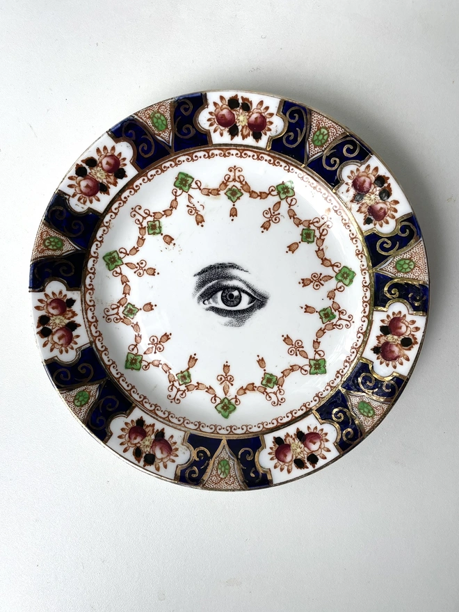 a very ornate vintage plate with high pattern and in the centre is a vintage black and white illustration of an eye