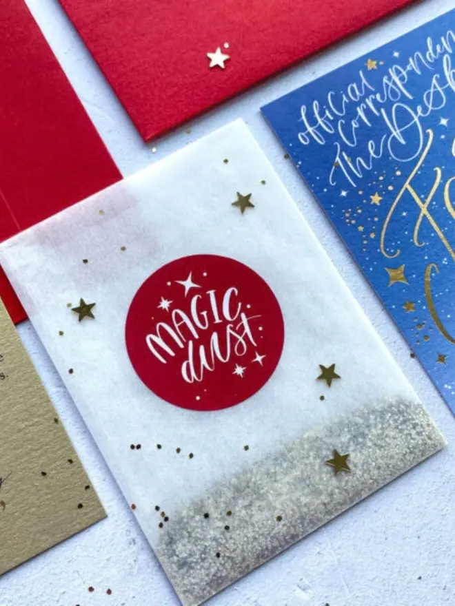 A glassine packet of silver glitter with a red "Magic Dust" sticker and gold confetti stars.