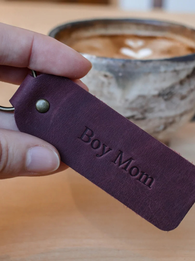 mother's day leather keyring. a hand holding a brown keyring embossed with 'boy mom'.