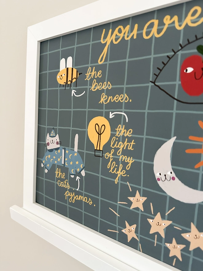 A close up of a positive affirmation print including the text 'the bees knees', 'the light of my life' and 'the cat's pyjamas' with a drawing of a bee, a lightbulb and a cat in pyjamas. 