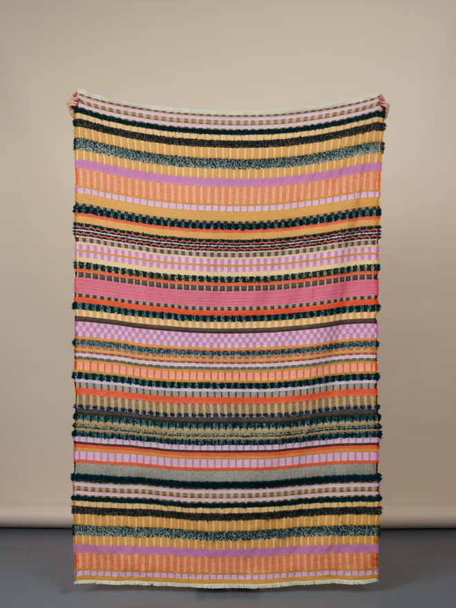  aednat lambswool blanket. a multi coloured patterned blanket photographed against a plain wall.