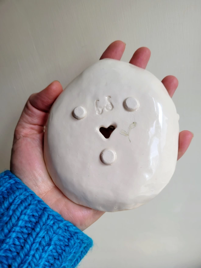 hand holding a ceramic pottery soap dish showing the underneath with 3 little feet heart shape cut out and a seedling leaf illustration