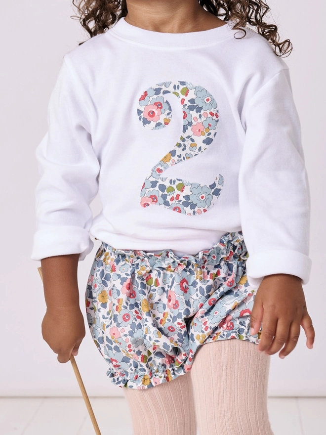 a 2 year old girl wearing a white birthday t-shirt with a number 2 cut from liberty floral print on the front