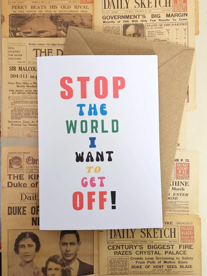 A mindful empathetic greeting card that says stop the world I want to get off in colourful fonts on a white card places on a background of old newspapers