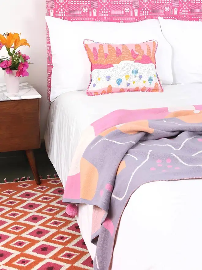 Evil Eye Flatweave Rug, a colourful rug in a bedroom. It is accompanied by other colourful bedding items. 