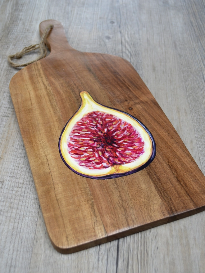 A wooden serving board with a handpainted design of a ripe fig