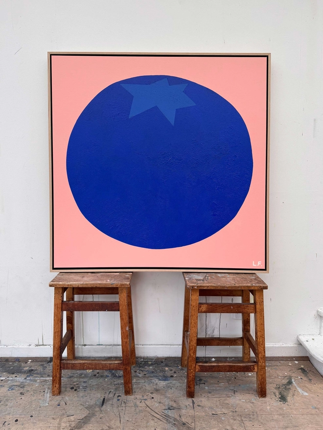 Large painting of a giant blueberry propped up on wooden stoold
