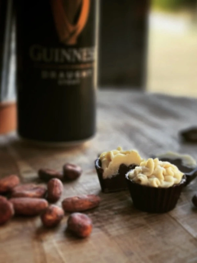 Irish Stout Chocolate Cups Made With Real Stout (Box Of 4), some chocolate cups sitting on a wooden surface. They are accompanied by nuts and a Guinness. 