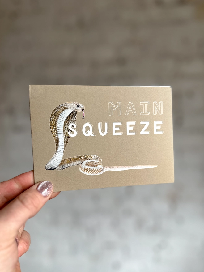 a beige greetings card featuring an illustration of a cobra with the text “main squeeze”