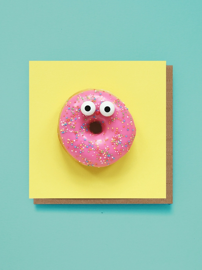 A surprised pink glazed doughnut on a zingy yellow backdrop 