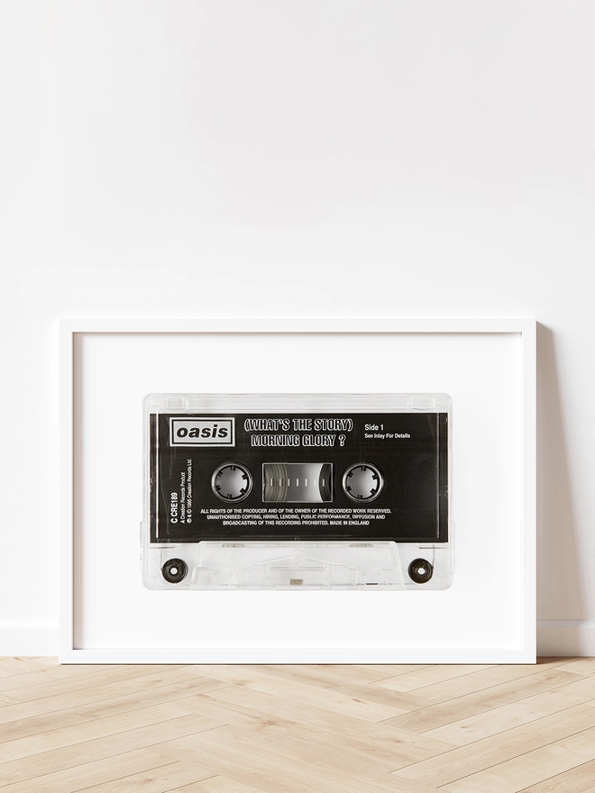 oasis whats the story morning glory cassette tape print. framed print propped up against white wall and wooden floor.