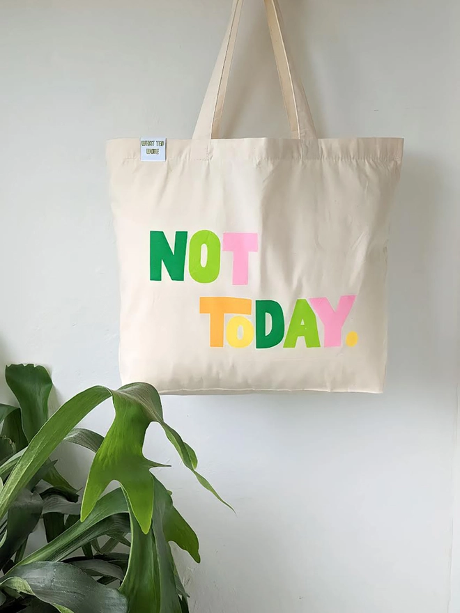 A hanging natural canvas tote bag with multi coloured Not Today slogan.