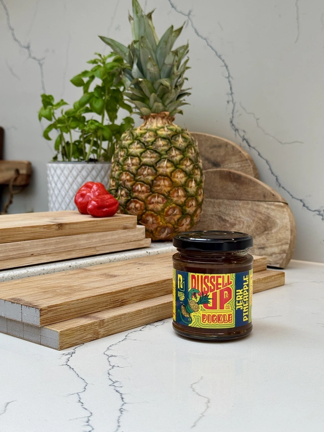father's day pickles - spice set. a jar of jerk pineapple pickle photographed next to a chopping board with a pineapple.