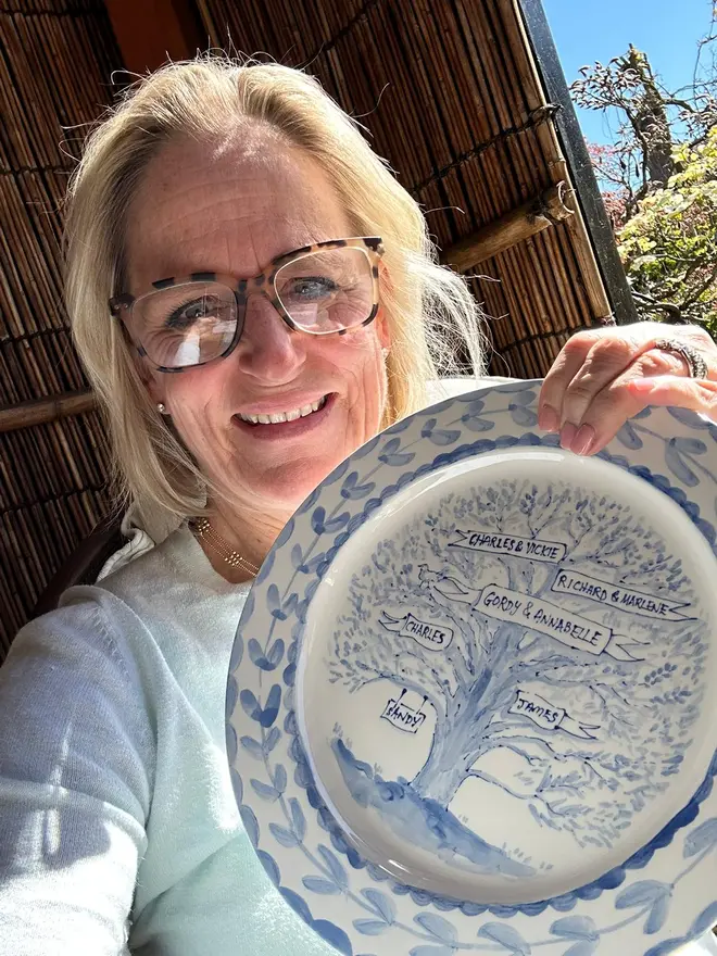 Customer holds her blue and white family tree plate, handpainted blue on white depicting a tree holding the family names in the branches