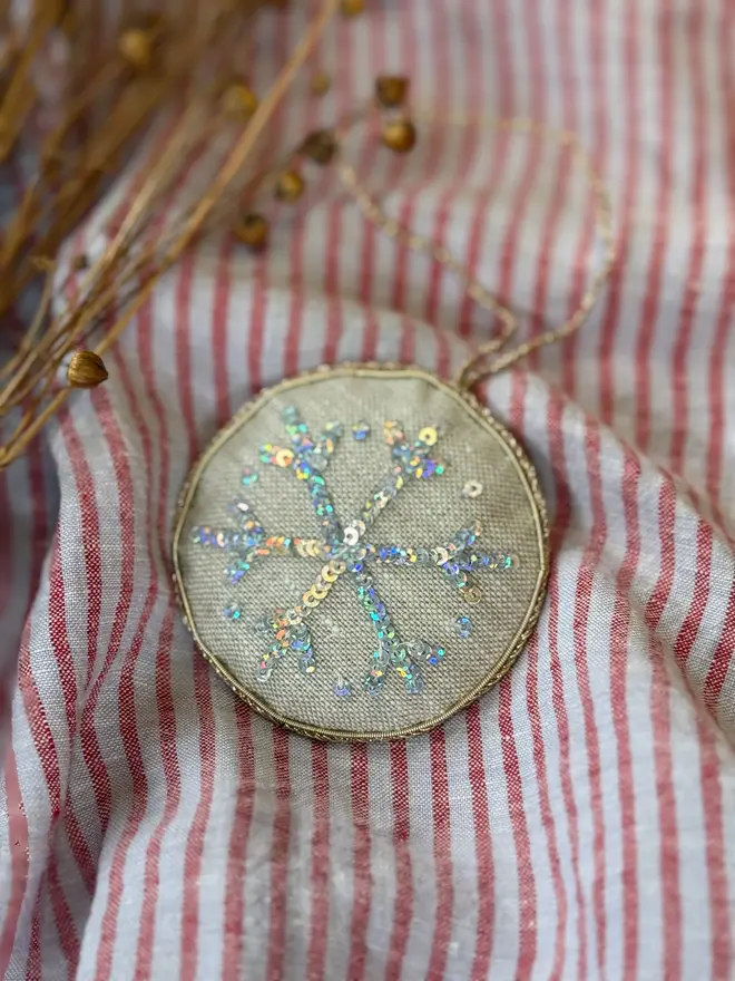 embroidered linen sparkly snowflake decoration. snowflake hanging ornament photographed against pinstripe fabric backdrop.
