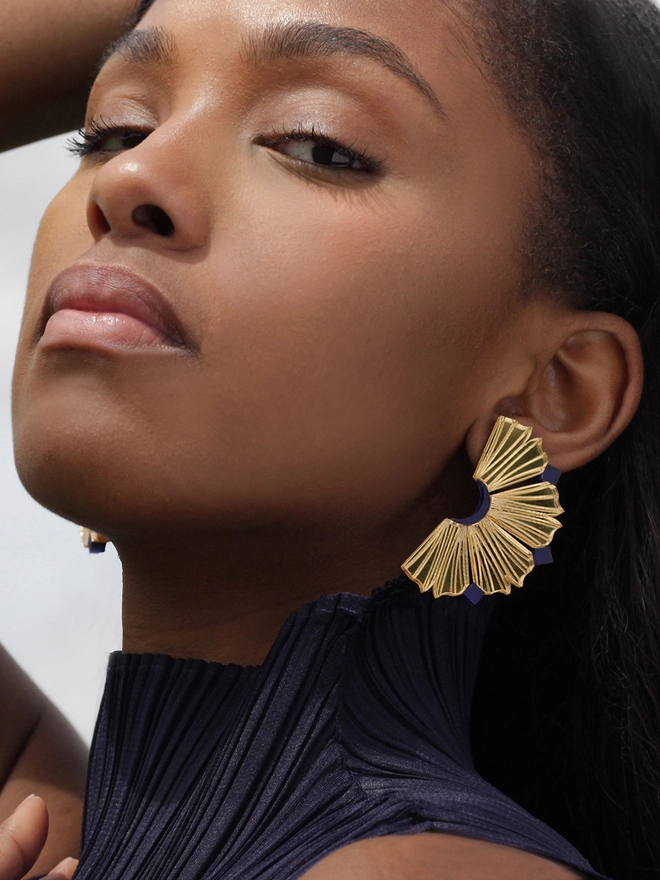 A close portrait of a model wearing Nalla Earrings- shapes resembles the coral walls of Lamu Island and also a slice pineapple. The model is wearing high neck pleated top.