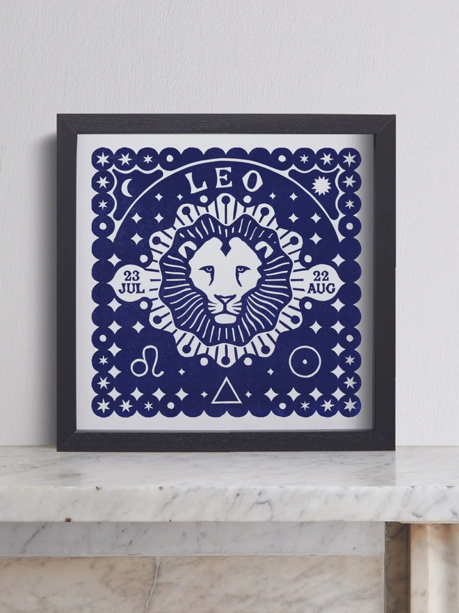 leo zodiac lino cut. a linocut lion and zodiac symbols printed on a blue background.