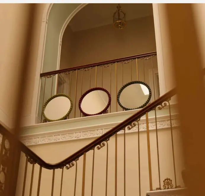 Three round oversized bobbin mirrors, in different colours displayed at the top of a grand stair case. 