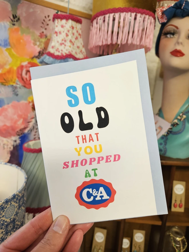 A photograph of the front of a humorous A6 greeting card illustrated using brightly coloured text and the retro shop logo. The text says so old you shopped at C&A