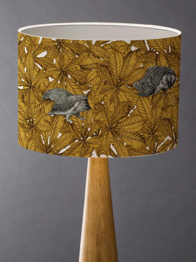 Handmade lampshade featuring cosy hedgehogs nestled among autumnal yellow leaves, creating a warm and whimsical woodland design.